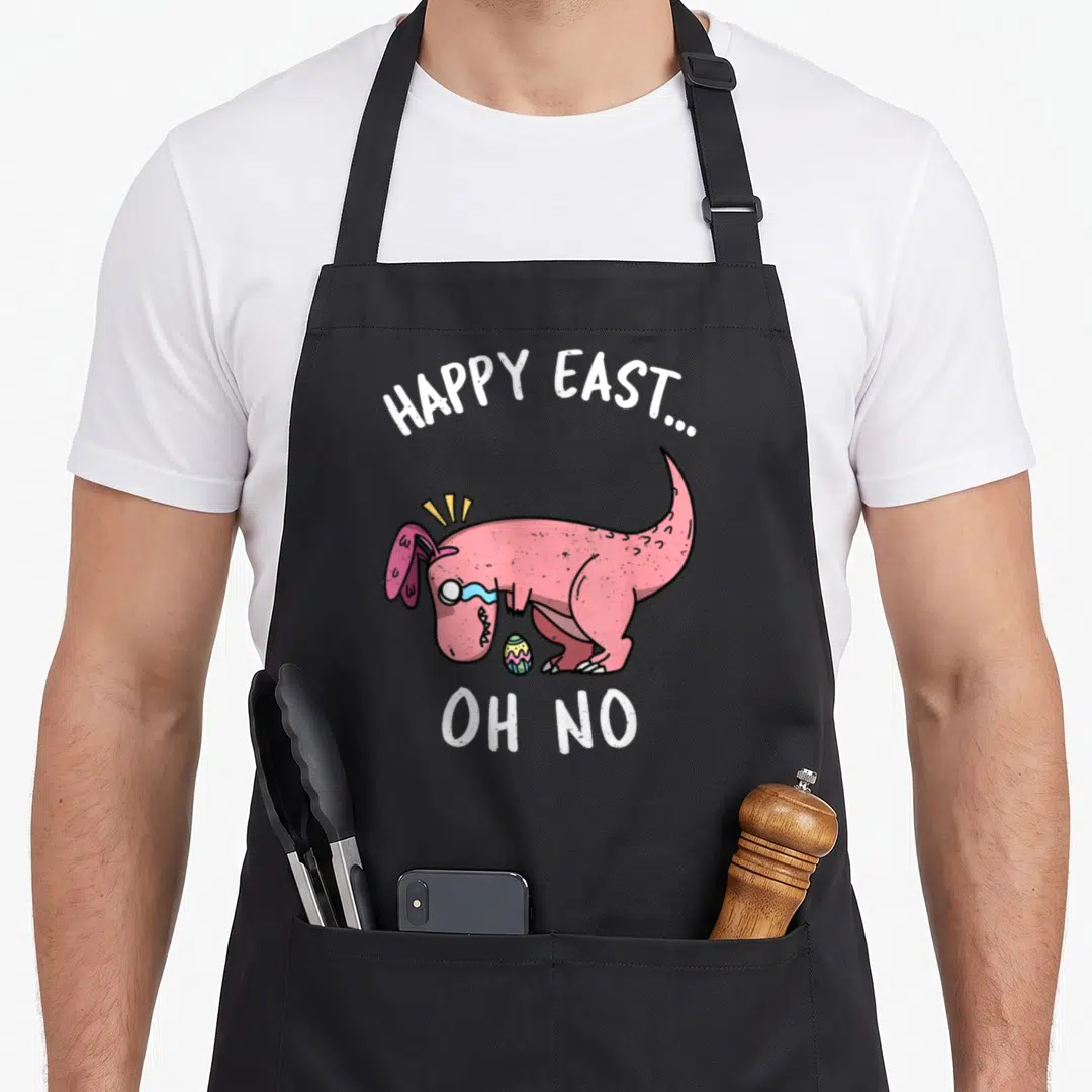 East easter apron - Pink cartoon dinosaur with bunny ears crying over egg under HAPPY EAST... OH NO text — shown on a black cotton canvas apron against a white background