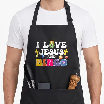 Jesus bingo aprons - I Love Jesus And Bingo text with crowned green ball and colorful numbered bingo balls — shown on a black cotton canvas apron against a white background
