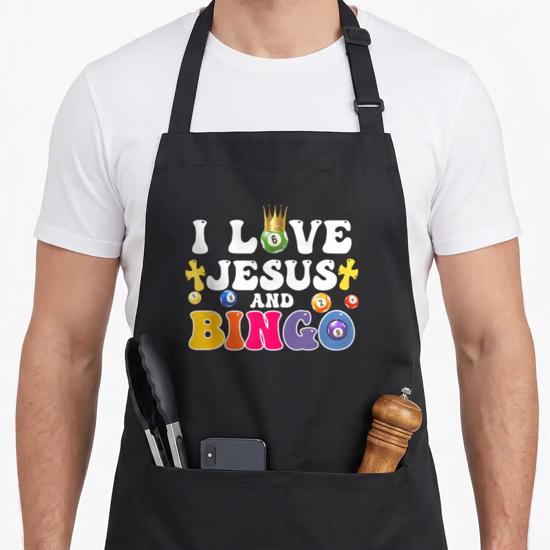 Jesus bingo aprons - I Love Jesus And Bingo text with crowned green ball and colorful numbered bingo balls — shown on a black cotton canvas apron against a white background