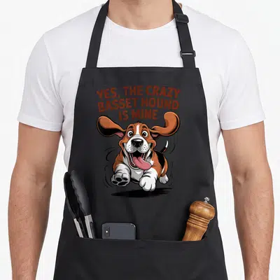 Cartoon cooking with dog apron - Running cartoon Basset Hound with YES THE CRAZY BASSET HOUND IS MINE text — shown on a black cotton canvas apron against a white background