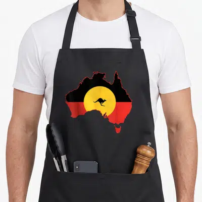 Flag aboriginal apron - Australia map filled with black red and yellow flag design containing a central yellow circle — shown on a black cotton canvas apron against a white background