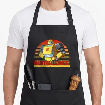 Portrait stripe apron - Cartoon Bumblebee with striped sun and red BUMBLEBEE text — shown on a black cotton canvas apron against a white background