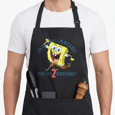 Squarepant 2nd apron - SpongeBob running with I'M READY! text and 2ND BIRTHDAY graphic — shown on a black cotton canvas apron against a white background