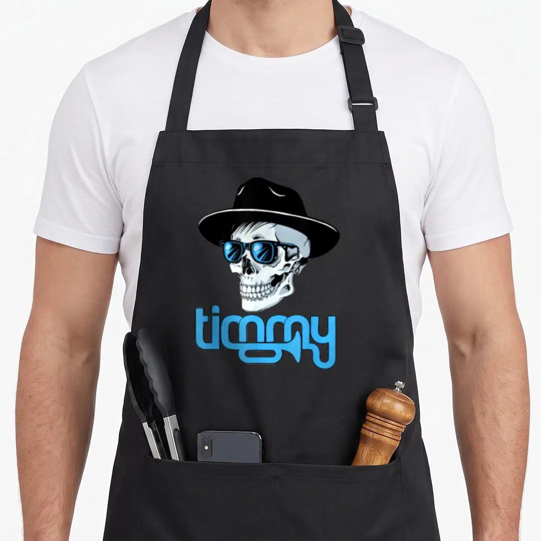 Timmy trumpet apron - Cartoon skull in hat and blue sunglasses above blue text reading timmy — shown on a black cotton canvas apron against a white background