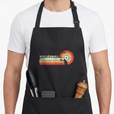 Cute volleyball apron - VOLLEYBALL text over red orange yellow stripes with player silhouette in concentric semi-circles — shown on a black cotton canvas apron against a white background