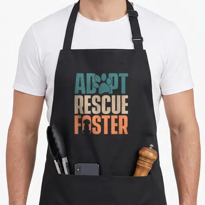Adoption grill rescue apron - Distressed Adopt Rescue Foster text with paw print and dog silhouette in teal beige orange — shown on a black cotton canvas apron against a white background