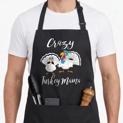Mama thanksgiving apron - Two cartoon turkeys with Crazy Turkey Mama text in white script — shown on a black cotton canvas apron against a white background