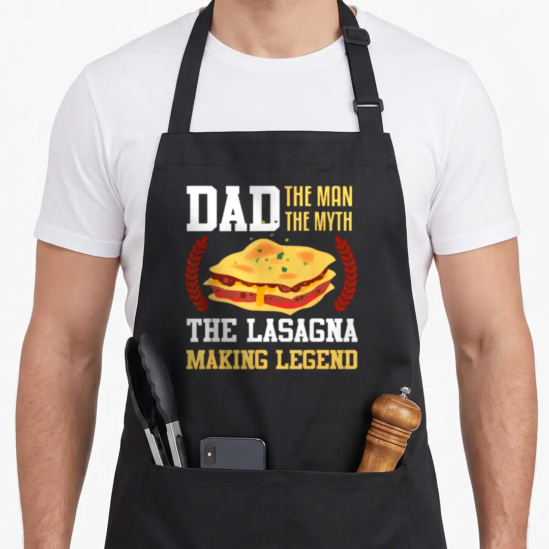 Lasagna makers apron - Cartoon lasagna slice flanked by red wreaths with stacked white and yellow text — shown on a black cotton canvas apron against a white background