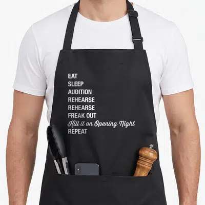 Geek theatre apron - White stacked text reading EAT SLEEP AUDITION REHEARSE FREAK OUT Kill it on Opening Night REPEAT — shown on a black cotton canvas apron against a white background