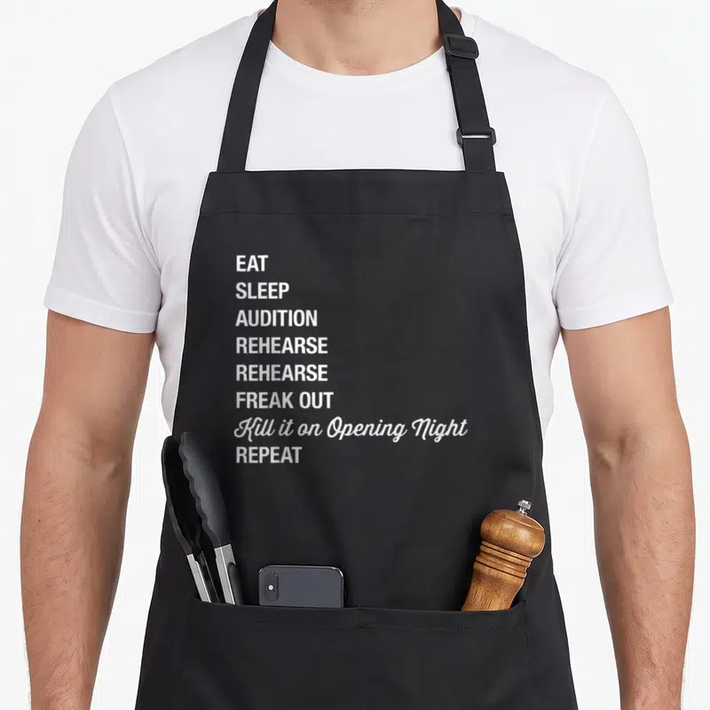 Geek theatre apron - White stacked text reading EAT SLEEP AUDITION REHEARSE FREAK OUT Kill it on Opening Night REPEAT — shown on a black cotton canvas apron against a white background