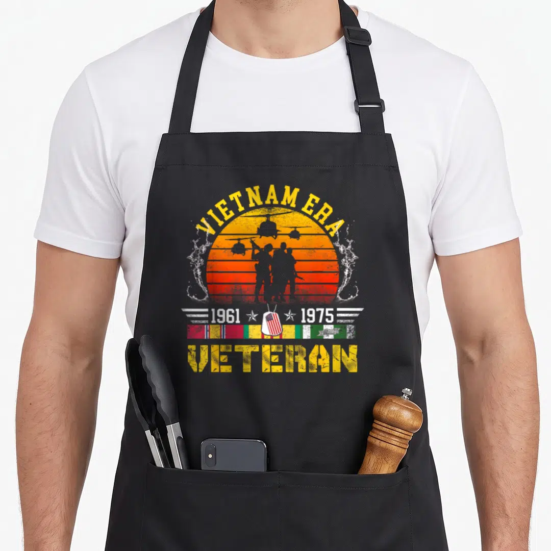 Veteran retired soldier apron - Distressed Vietnam Era 1961 1975 veteran text with soldier silhouettes and ribbon bar — shown on a black cotton canvas apron against a white background