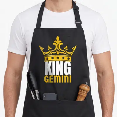 Gemini king apron - Yellow crown above white KING and yellow Gemini text — shown on a black cotton canvas apron against a white background