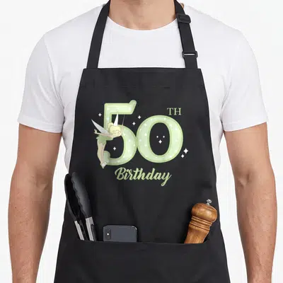 Peter birthday apron - Tinker Bell overlapping green 50TH Birthday text with white sparkles — shown on a black cotton canvas apron against a white background