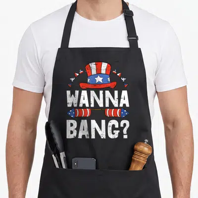 Bang firework 4th of july apron - Uncle Sam hat above WANNA BANG text flanked by red white blue rockets in distressed — shown on a black cotton canvas apron against a white background