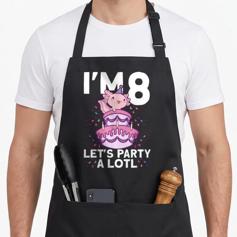 Axolotl bday birthday apron - Pink axolotl on two-tier cake with party text and confetti — shown on a black cotton canvas apron against a white background