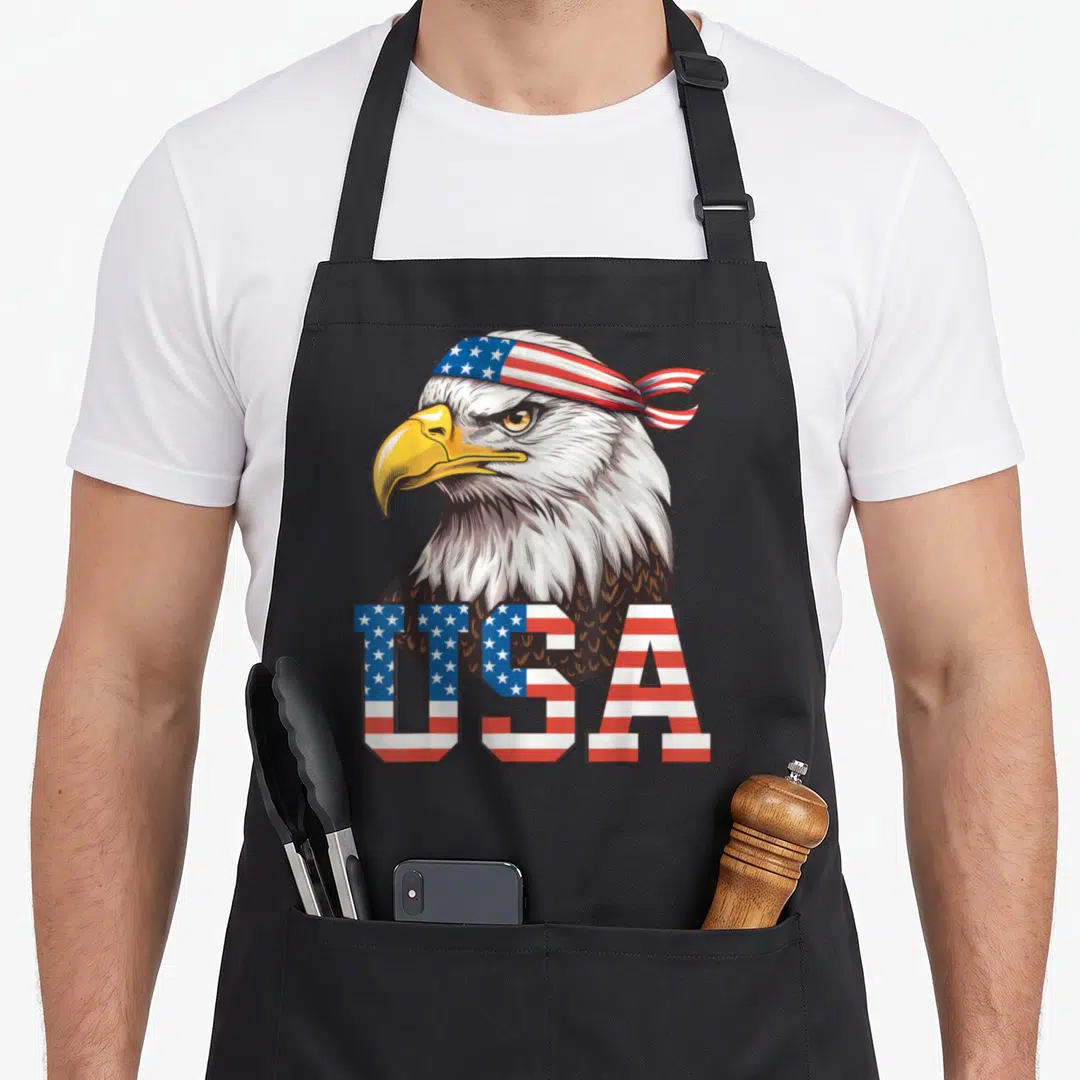 Eagle patriotic american flag apron - Bald eagle wearing red white blue flag bandana with USA text filled in flag — shown on a black cotton canvas apron against a white background