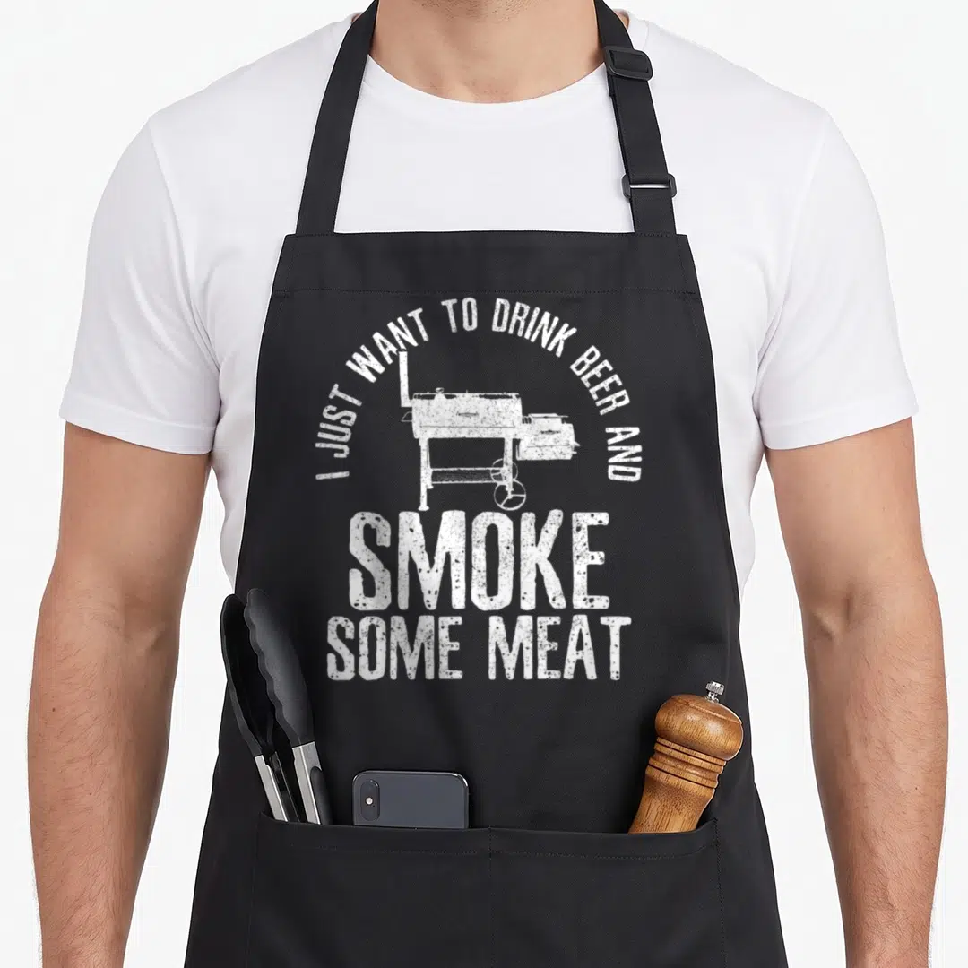 Drink beer meat aprons - White distressed text and smoker grill graphic on black fabric — shown on a black cotton canvas apron against a white background