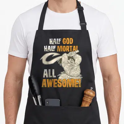 Maui distressed apron - Cartoon character holding a large hook with stacked text reading HALF GOD HALF MORTAL ALL — shown on a black cotton canvas apron against a white background