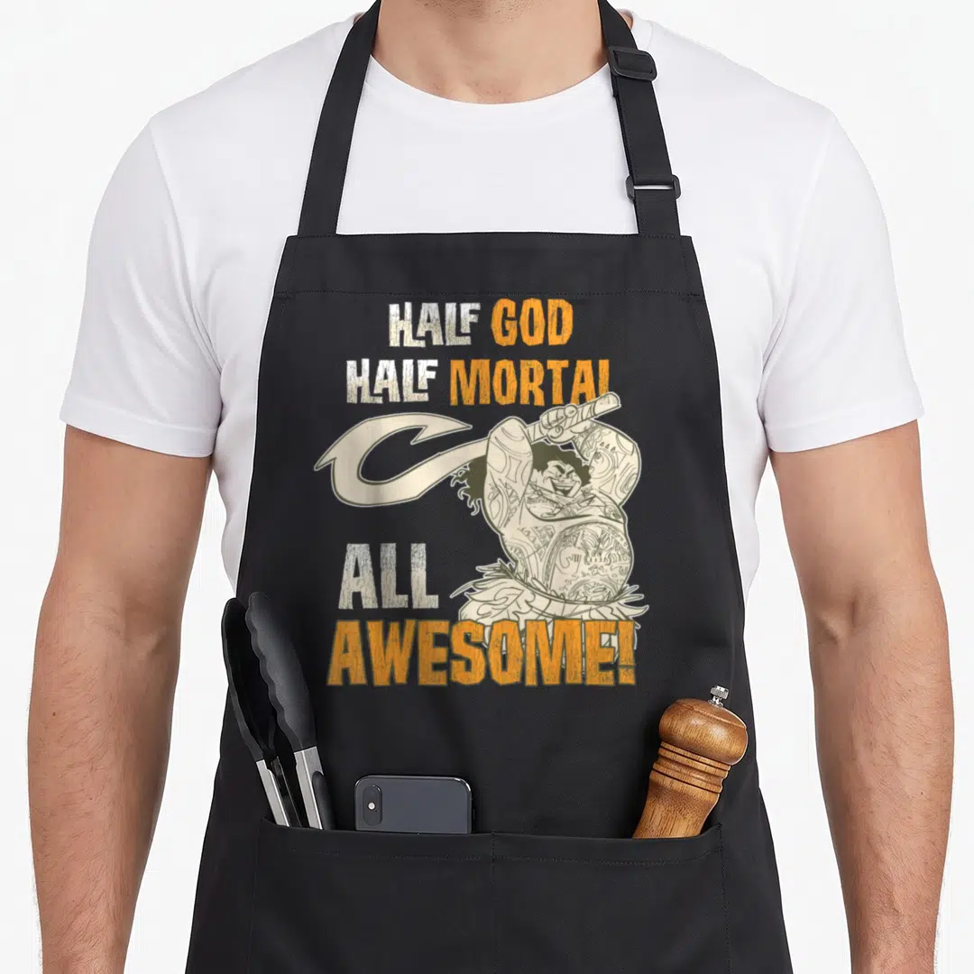 Maui distressed apron - Cartoon character holding a large hook with stacked text reading HALF GOD HALF MORTAL ALL — shown on a black cotton canvas apron against a white background