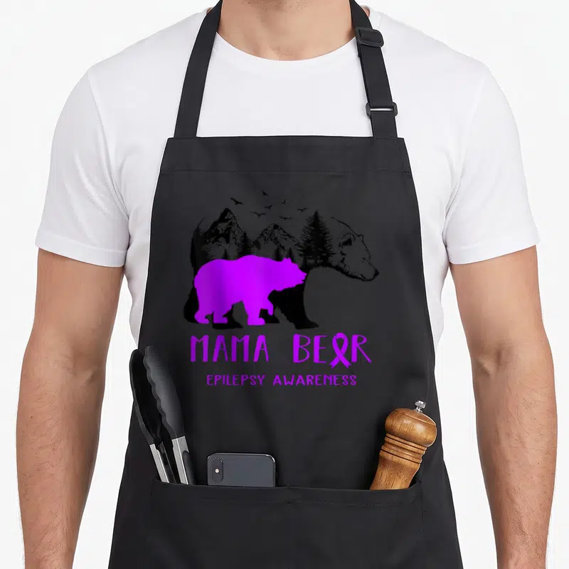 Epilepsy mama bear apron - Purple MAMA BEAR text with ribbon, overlapping purple and black bears containing mountain — shown on a black cotton canvas apron against a white background