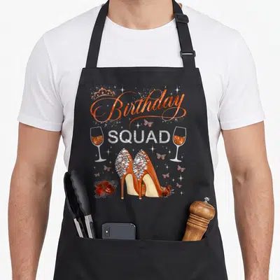 Squad heel butterfly apron - Rhinestone SQUAD text, jeweled ruby heels, champagne glasses, butterflies, and roses — shown on a black cotton canvas apron against a white background