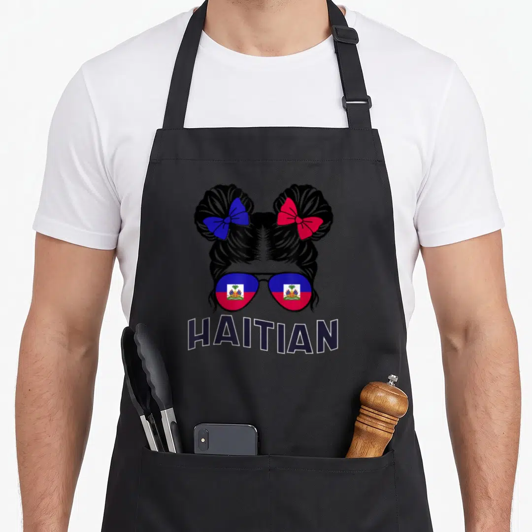 Haitian heritage pride apron - Woman silhouette with two buns, flag sunglasses, and HAITIAN text — shown on a black cotton canvas apron against a white background