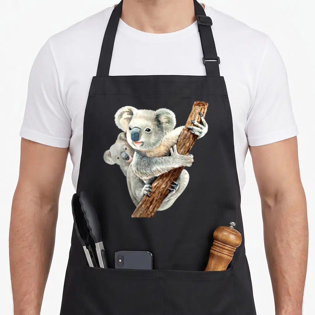 Realistic bear apron - Two watercolor koalas clinging to brown branch, smaller peeking from behind larger one — shown on a black cotton canvas apron against a white background