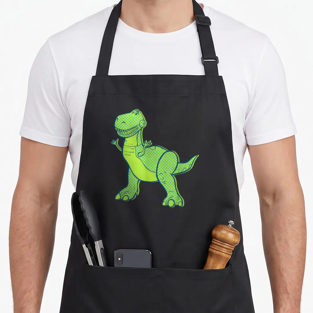 Halftone dog breed aprons - Lime green and blue cartoon T-Rex with blue halftone dots and outline — shown on a black cotton canvas apron against a white background