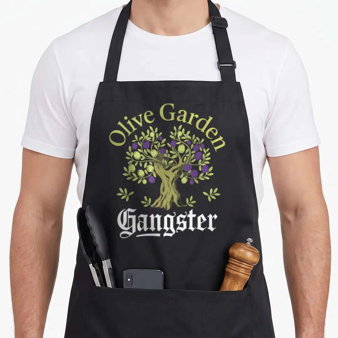 Gangster tree aprons - Olive Garden Gangster text over cartoon olive tree with purple and green fruit — shown on a black cotton canvas apron against a white background