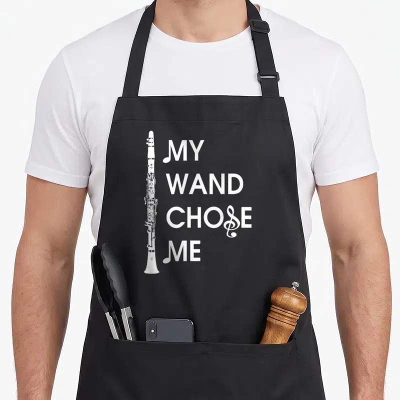 Wand clarinet apron - Vertical white clarinet next to stacked text MY WAND CHOSE ME with treble clef detail — shown on a black cotton canvas apron against a white background