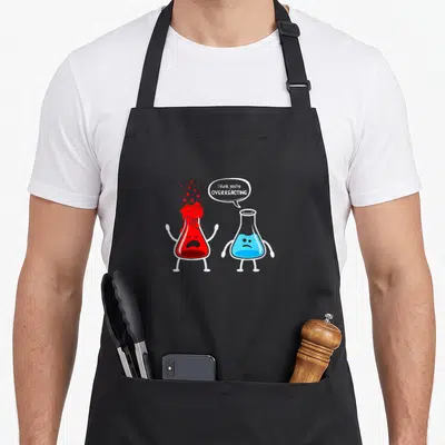 Funny overreacting chemistry apron - Cartoon red and blue beakers with speech bubble reading I think you're overreacting — shown on a black cotton canvas apron against a white background