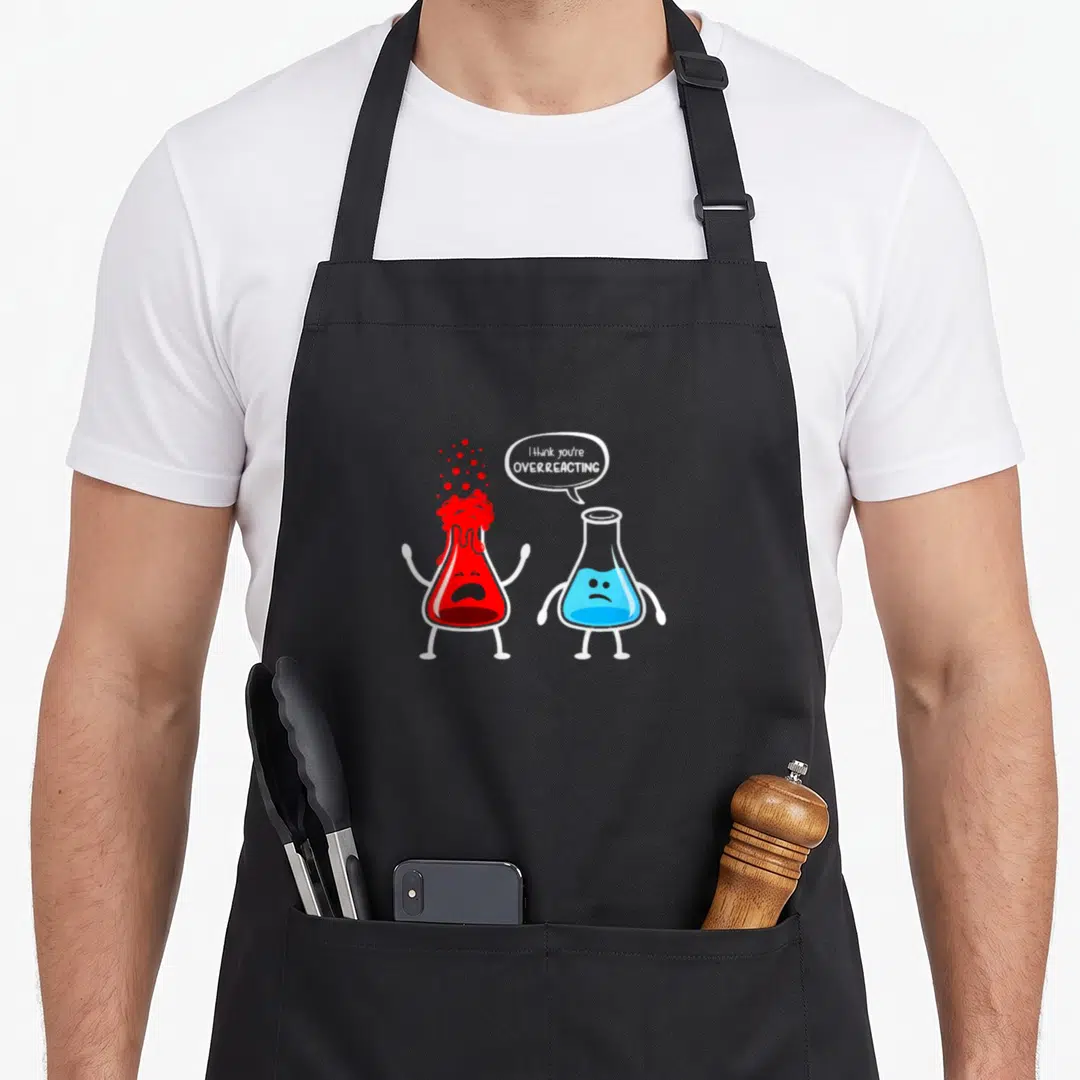 Funny overreacting chemistry apron - Cartoon red and blue beakers with speech bubble reading I think you're overreacting — shown on a black cotton canvas apron against a white background