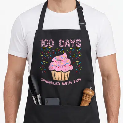 Sprinkled cupcake apron - Pink cupcake with rainbow sprinkles and 100 Days Sprinkled With Fun text — shown on a black cotton canvas apron against a white background