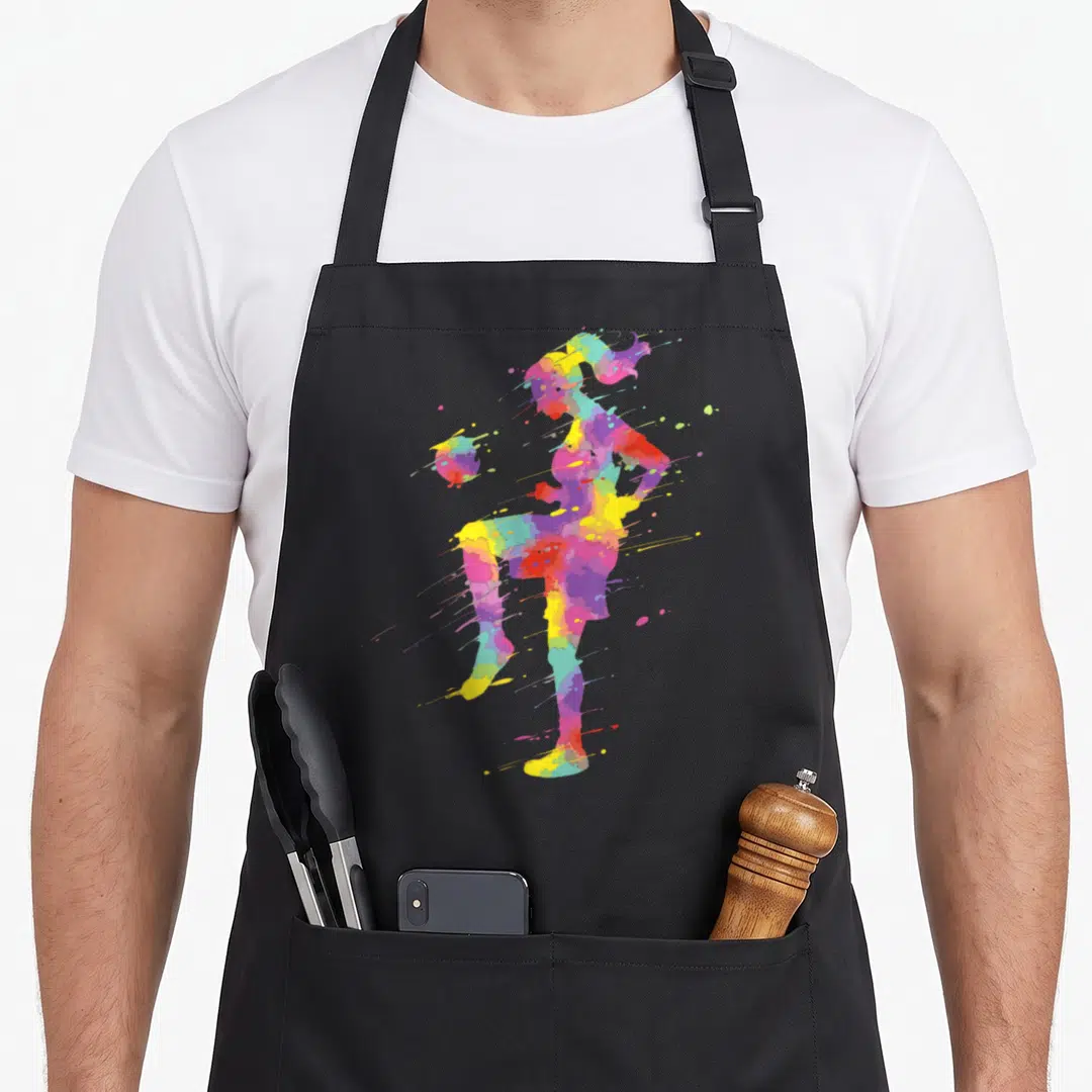 Funny soccer apron - Multicolored watercolor silhouette of a basketball player with paint splatters in yellow red blue — shown on a black cotton canvas apron against a white background