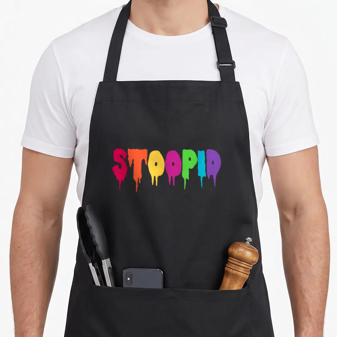Stoopid drip apron - Dripping rainbow text reading STOOPID in pink orange yellow purple green and blue — shown on a black cotton canvas apron against a white background