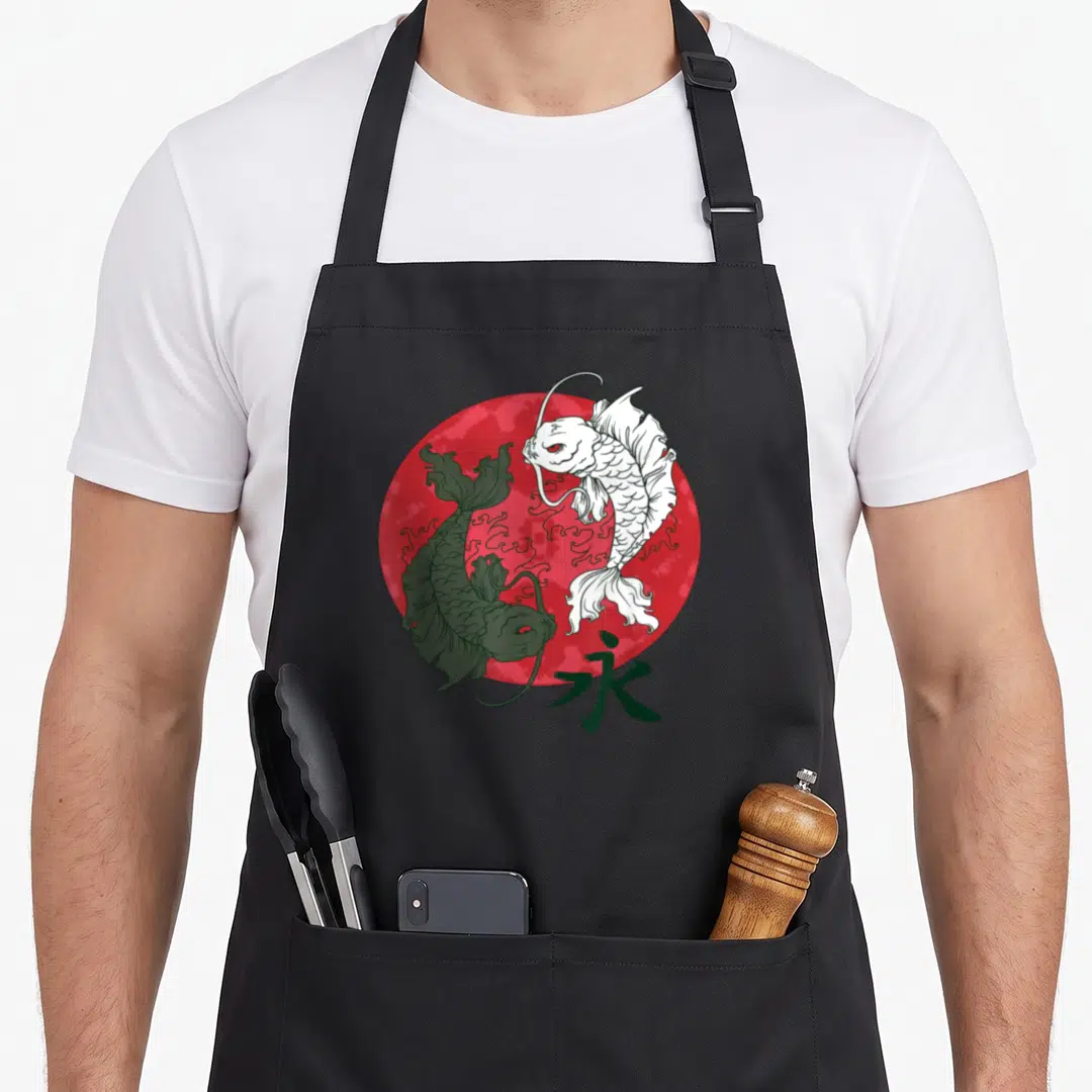 Yang fish apron - Two koi fish circling red sun with kanji character for eternity in line art — shown on a black cotton canvas apron against a white background