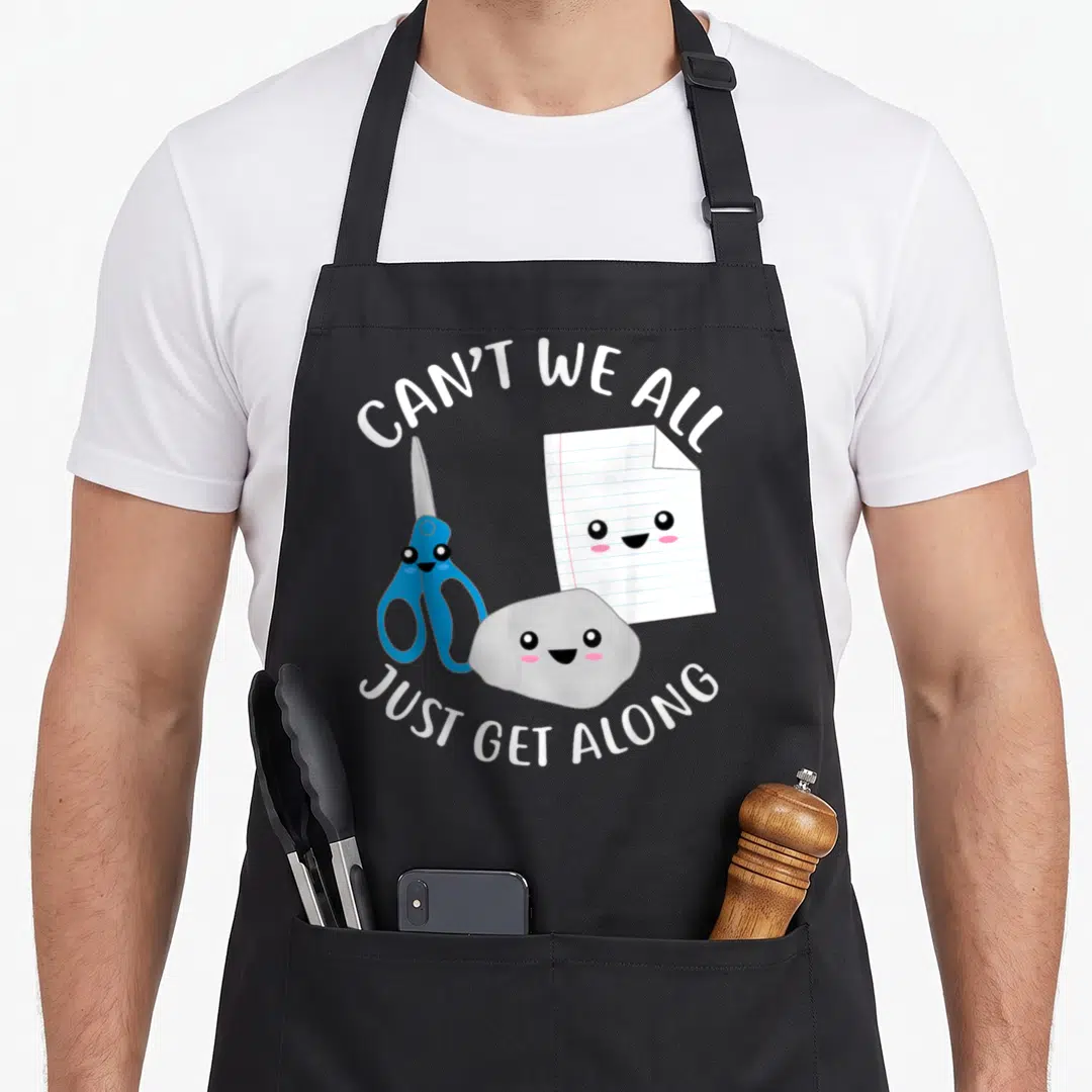 Kawaii paper apron - Three kawaii rock paper scissors characters with white text arcs on black background — shown on a black cotton canvas apron against a white background