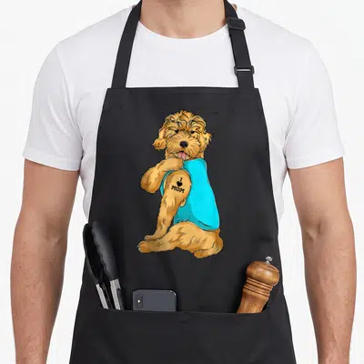 Tattoo goldendoodle apron - Cartoon golden dog in cyan shirt with black I heart MOM tattoo on upper arm — shown on a black cotton canvas apron against a white background