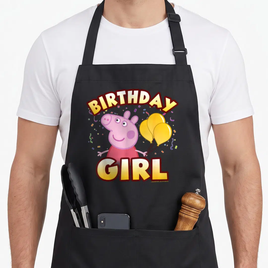 Confetti birthday apron - Pink pig holding three yellow balloons with BIRTHDAY GIRL text and confetti — shown on a black cotton canvas apron against a white background