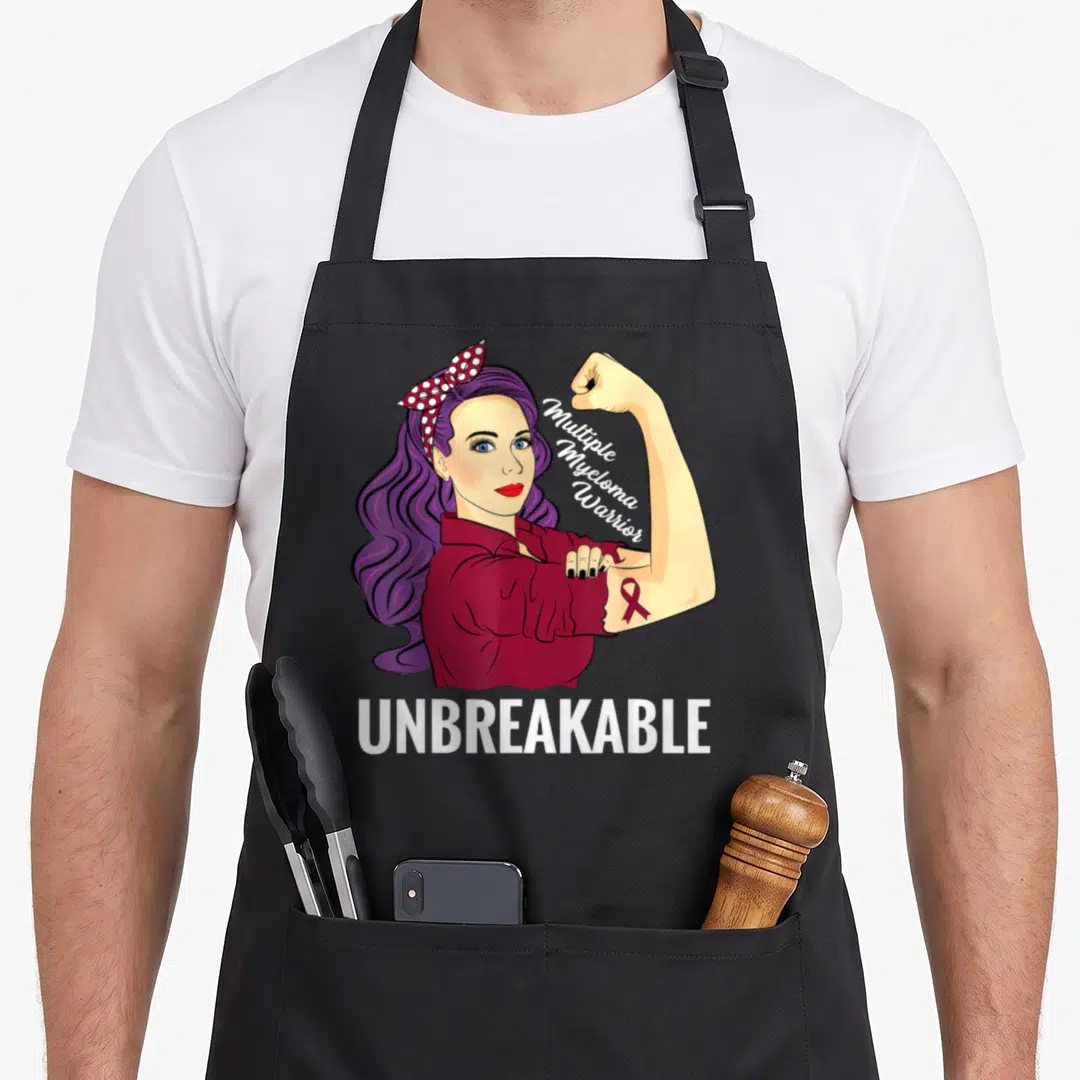Myeloma blood apron - Cartoon woman flexing arm with multiple myeloma warrior text and unbreakable label — shown on a black cotton canvas apron against a white background