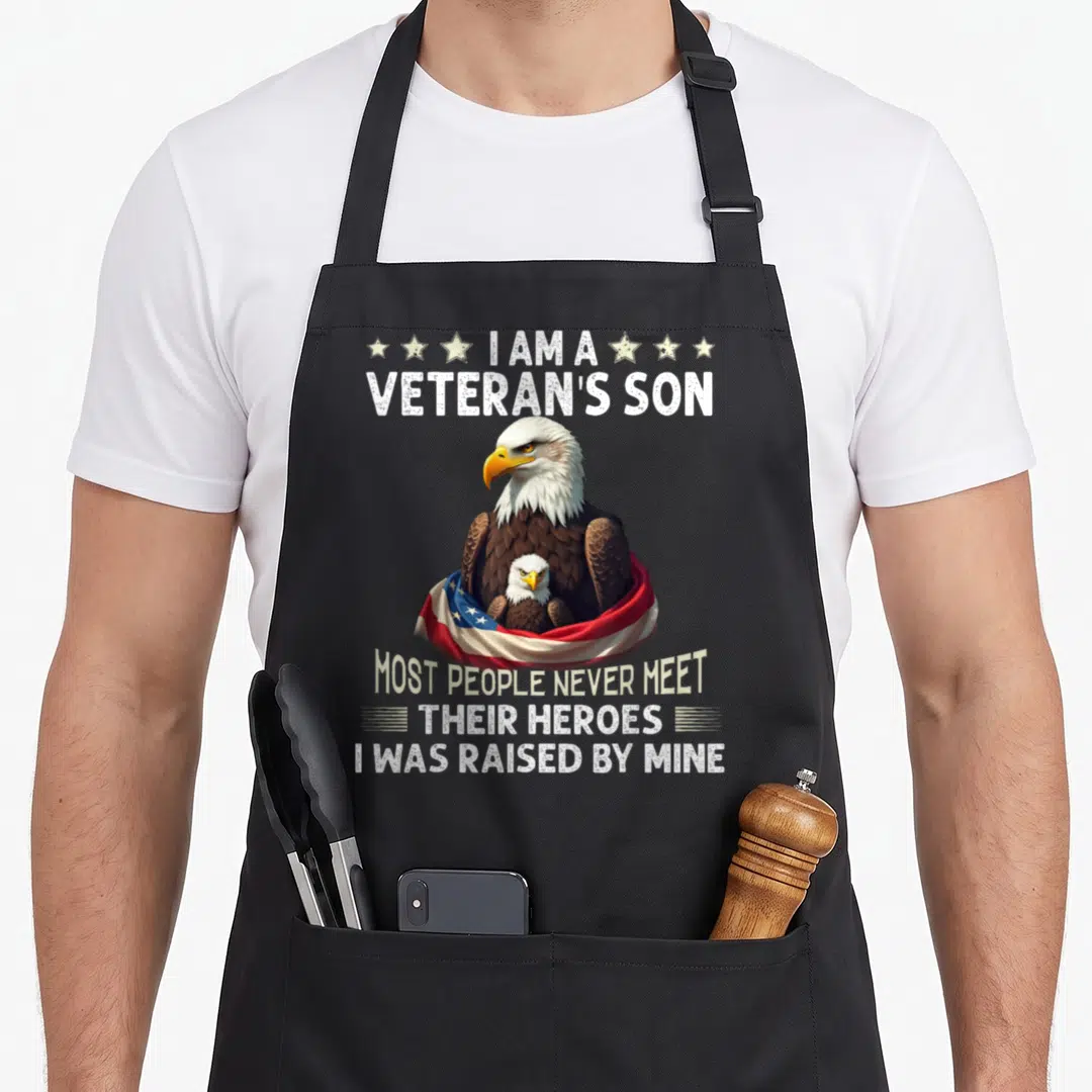 Veteran meet apron - Bald eagle protecting chick wrapped in flag with stars and white distressed text — shown on a black cotton canvas apron against a white background