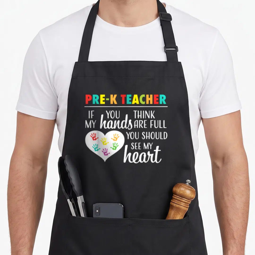 Pre appreciation teacher apron - Rainbow PRE-K TEACHER text next to white heart with six colorful handprints — shown on a black cotton canvas apron against a white background