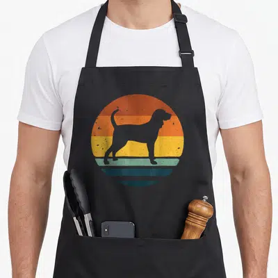 Cute coonhound dog apron - Grey dog silhouette on orange yellow and green striped circle — shown on a black cotton canvas apron against a white background