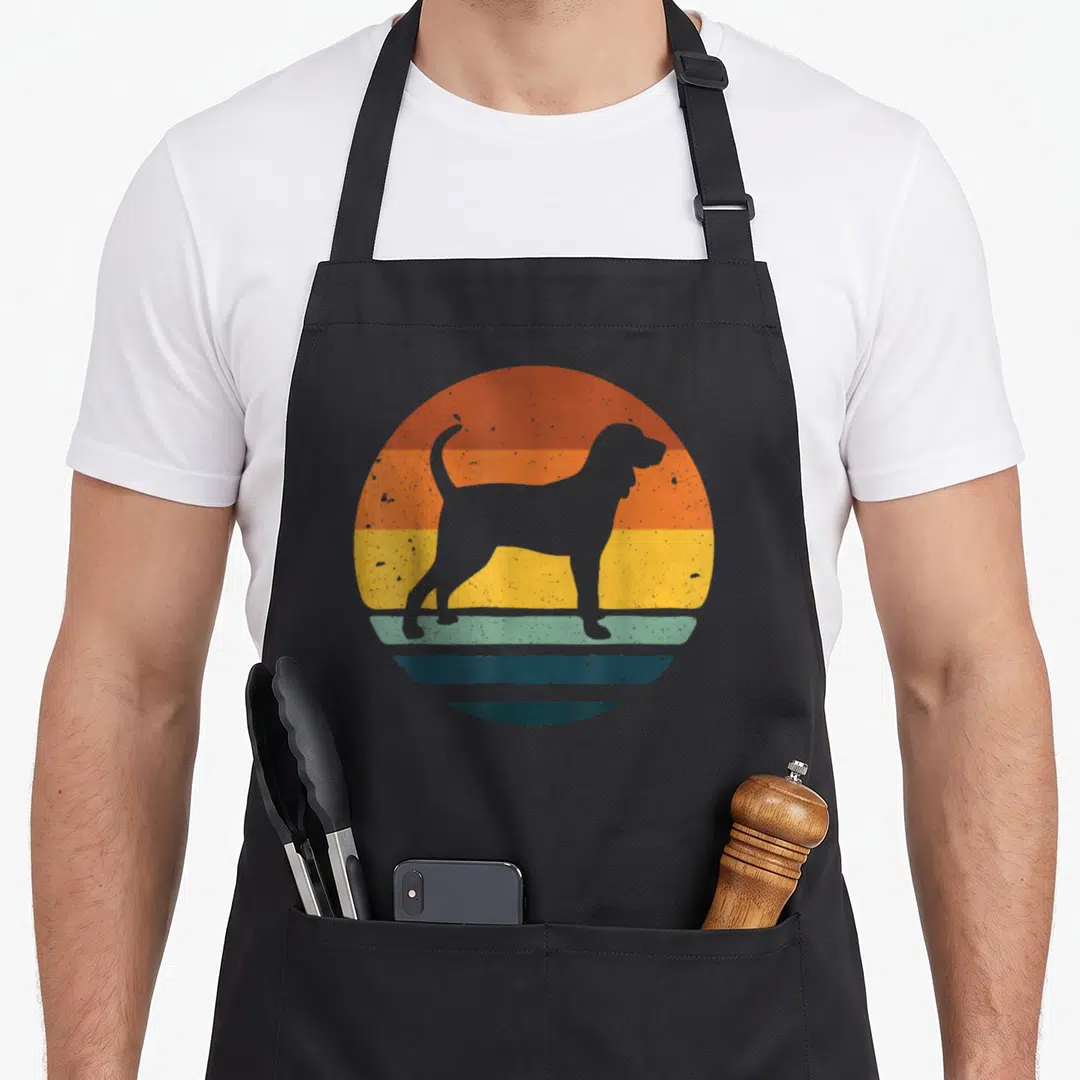 Cute coonhound dog apron - Grey dog silhouette on orange yellow and green striped circle — shown on a black cotton canvas apron against a white background