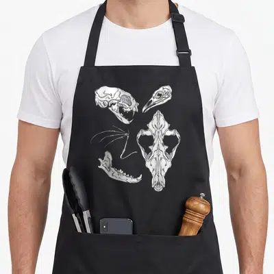 Witch gothic apron - White line art of four scattered animal skull fragments and bones on grey background — shown on a black cotton canvas apron against a white background