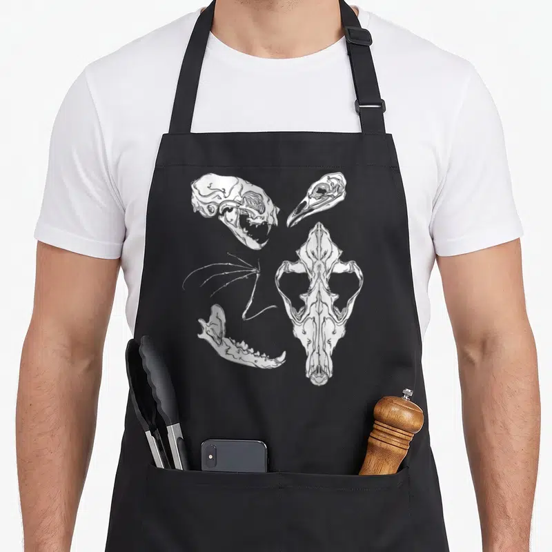 Witch gothic apron - White line art of four scattered animal skull fragments and bones on grey background — shown on a black cotton canvas apron against a white background