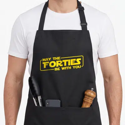 May 40th birthday apron - Yellow text May The Forties Be With You in Star Wars style font — shown on a black cotton canvas apron against a white background