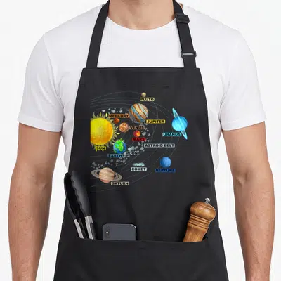 Solar science apron - Cartoon solar system with labeled planets and sun in colored boxes — shown on a black cotton canvas apron against a white background