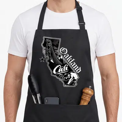 California oakland apron - California state outline with bridge skyline bear and Oakland Cali text in black white line — shown on a black cotton canvas apron against a white background