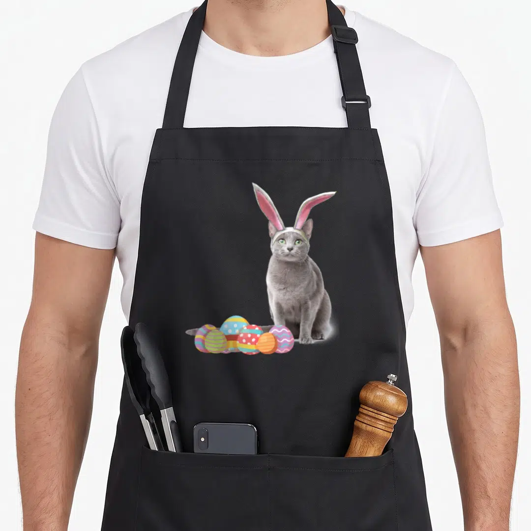 Easter russian aprons - Grey cat with pink bunny ears sitting beside colorful striped and polka dot Easter eggs — shown on a black cotton canvas apron against a white background